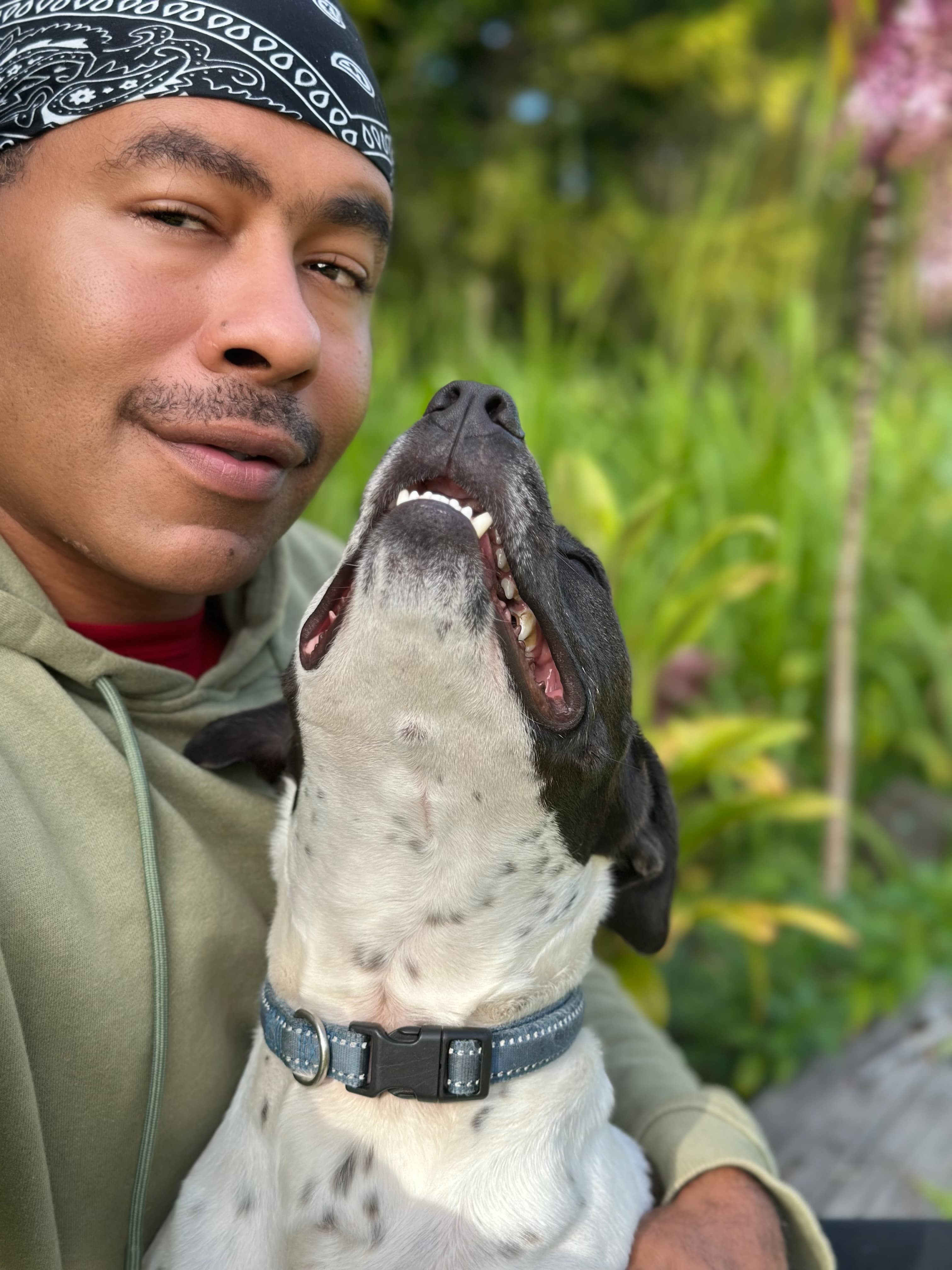 Jeffon laughing joyfully with his dog outdoors surrounded by lush greenery