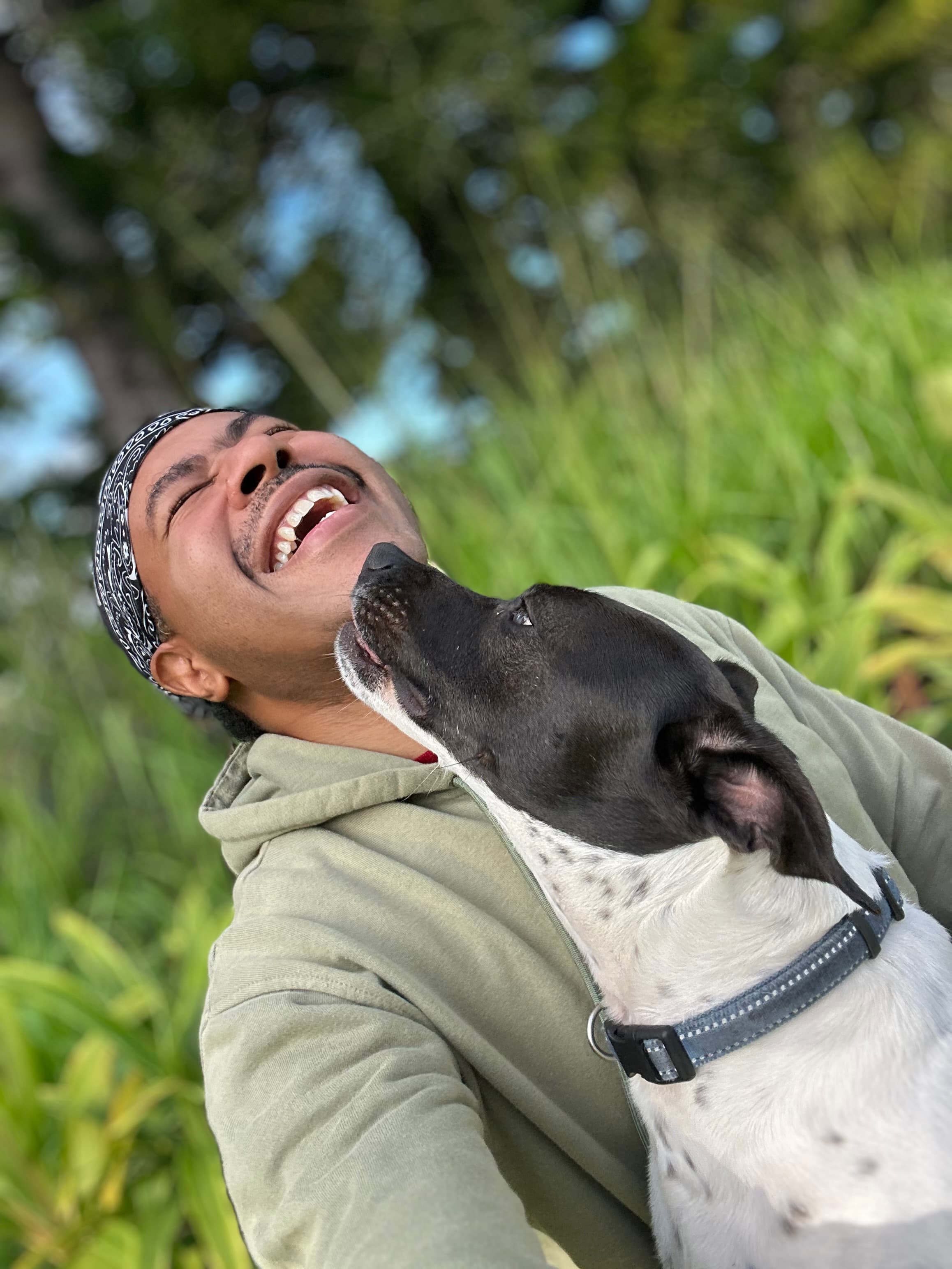 Jeffon laughing with pure joy as his dog gives him kisses, surrounded by lush tropical greenery